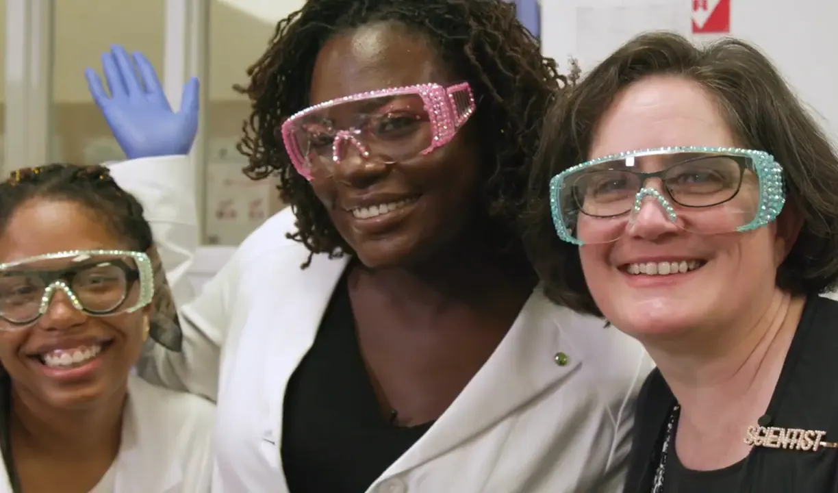 Dr. Raven Baxter smiling in pink goggles between Sydney Anderson and Dr. Sarah Bowman in the lab, from Nerdy Jobs Episode 1